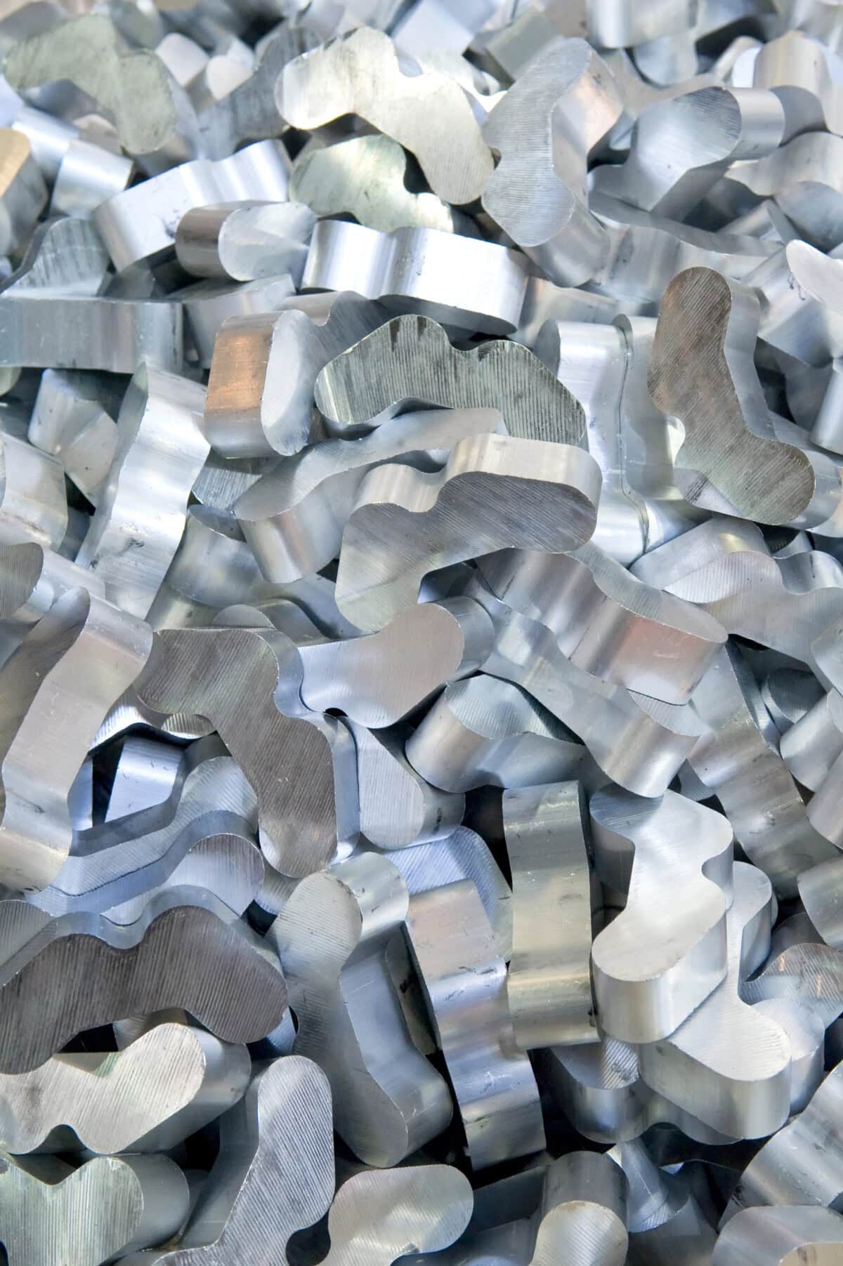 A pile of shiny, irregularly shaped silver metal pieces closely packed together, each with a curved and wavy form, reflecting light from different angles.