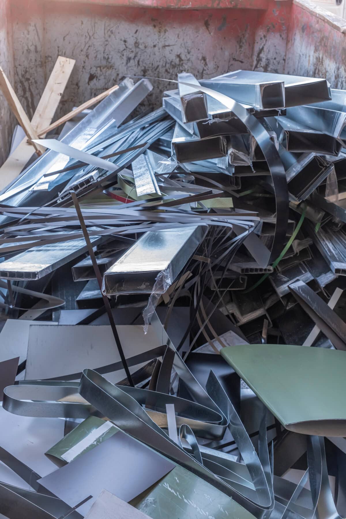 A pile of assorted metal scraps, including sheets, strips, and rectangular bars, inside a large container or dumpster.