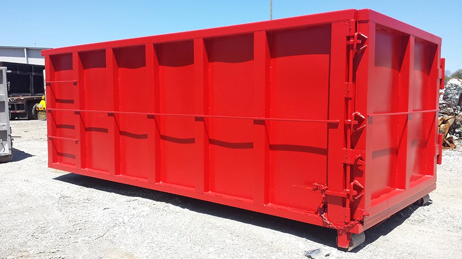 A large, bright red roll-off dumpster sitting on a gravel lot under a clear blue sky. The dumpster features reinforced steel panels and heavy-duty hinges on its side-hinged rear doors.